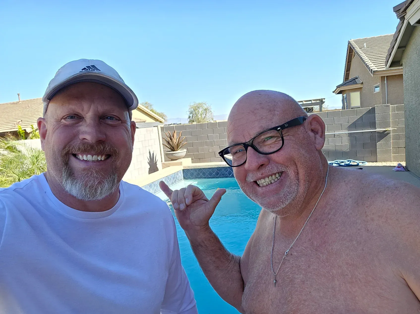 Two men are standing next to each other in front of a swimming pool.