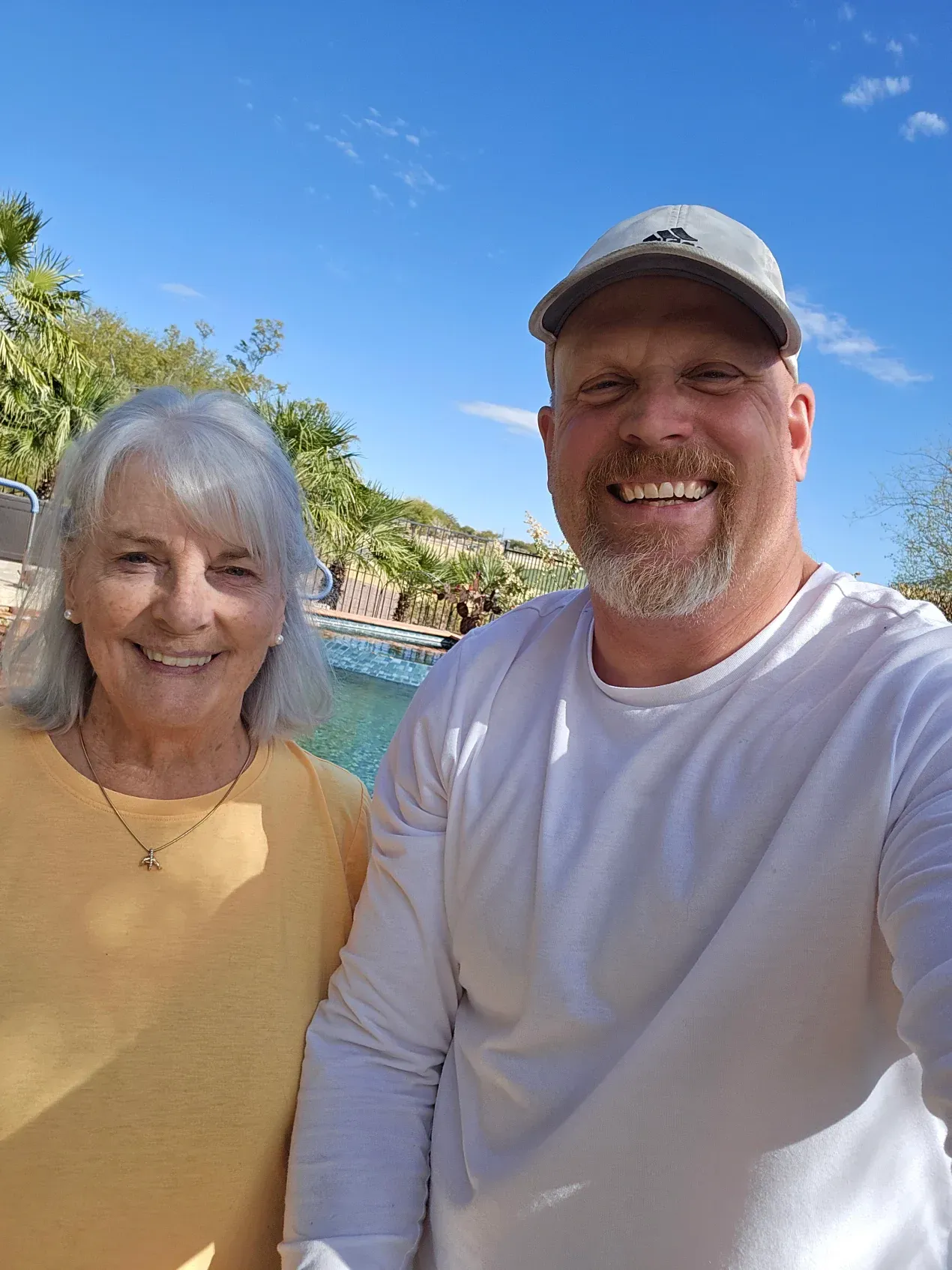 A man and a woman are posing for a selfie in front of a pool.