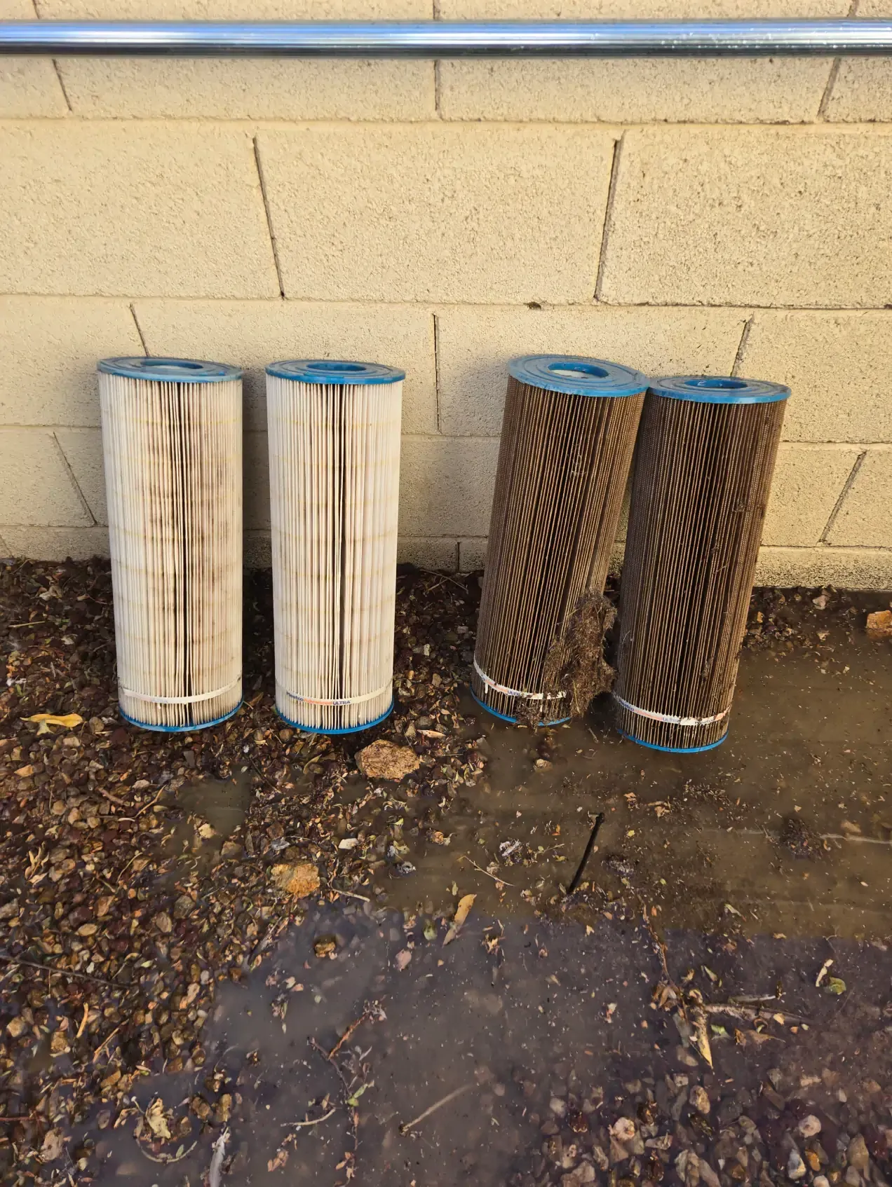 Three pool filters are sitting on the ground in front of a brick wall.