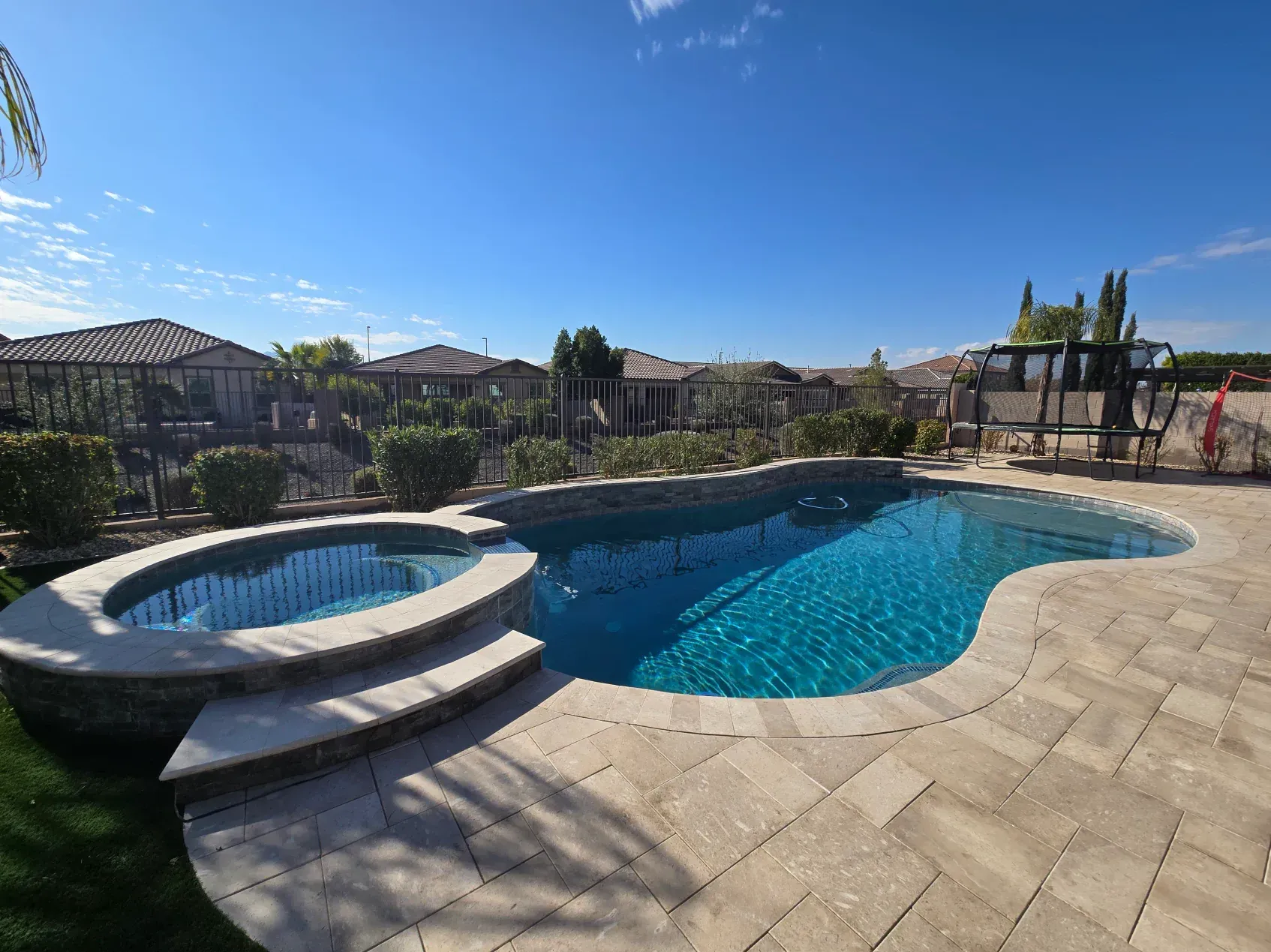 A large swimming pool with a hot tub in the backyard of a house.
