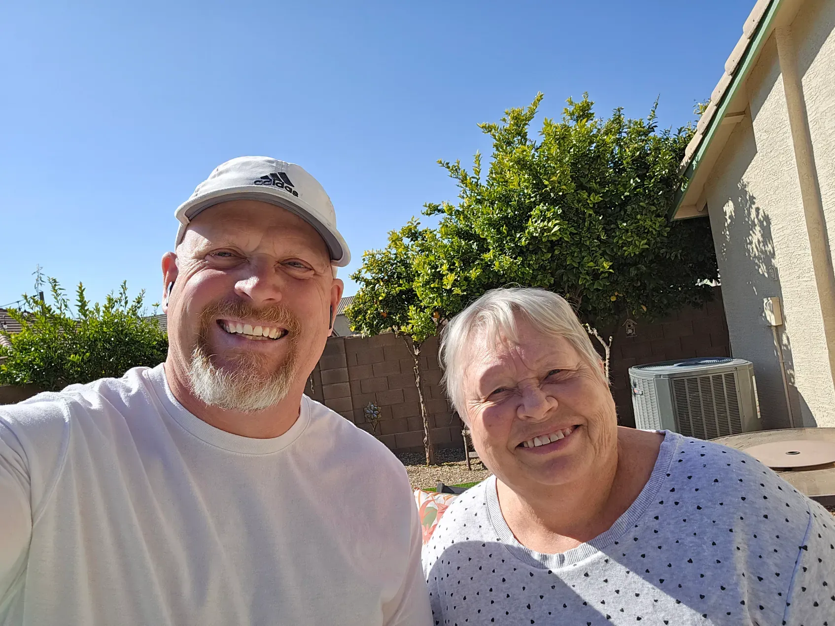 A man and a woman are posing for a selfie in front of a house.