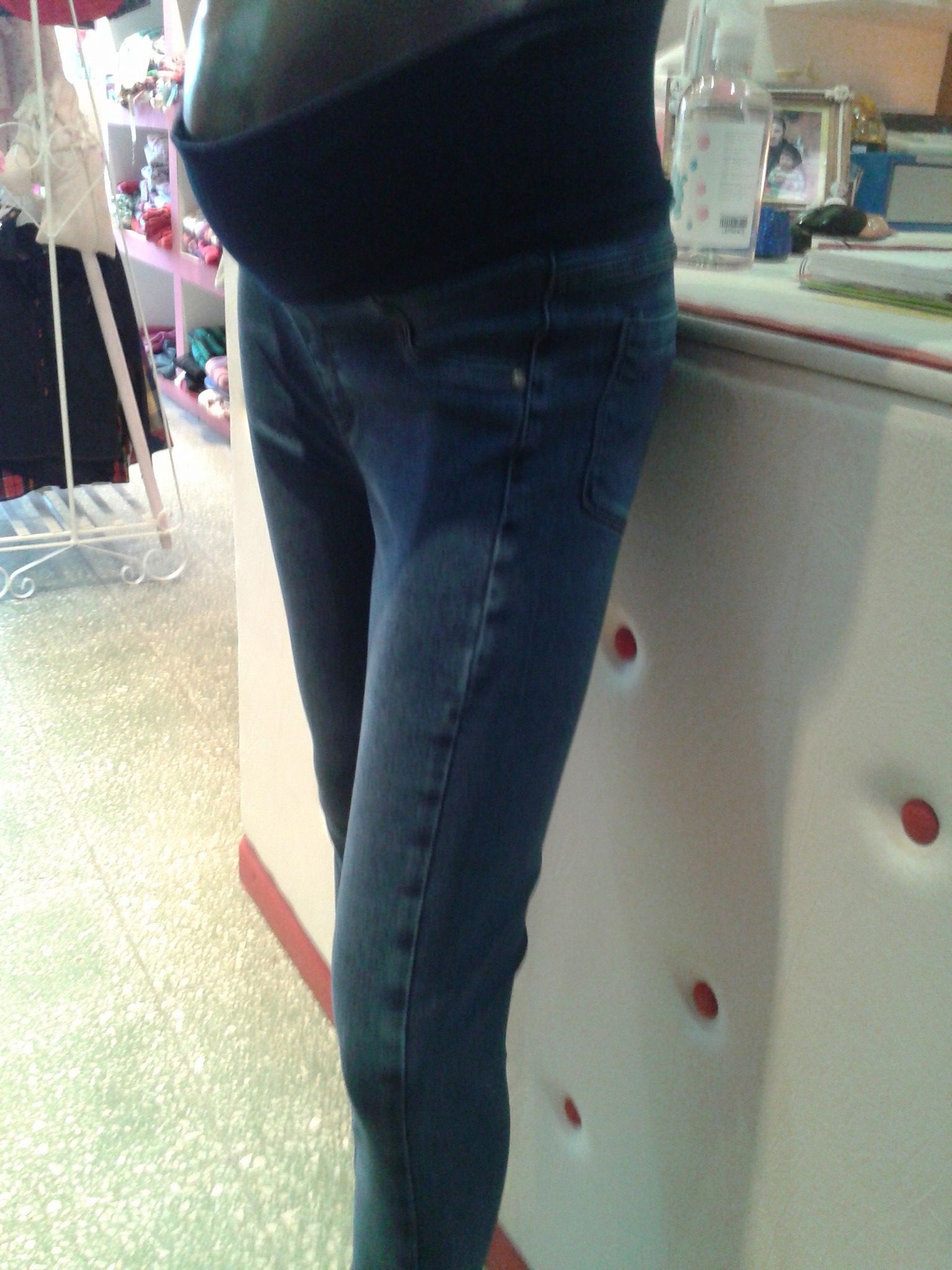 Una mujer embarazada que viste jeans azules está apoyada en un mostrador.