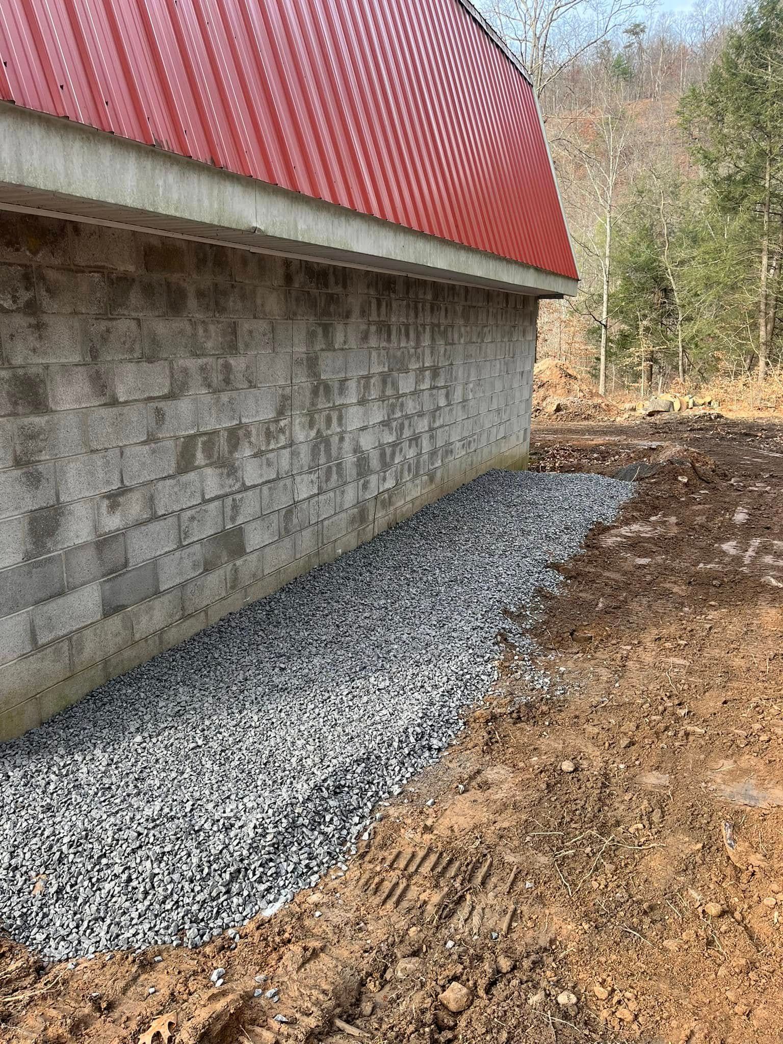 Gray cinder block building with a red arched roof, with a gravel bed at the base.