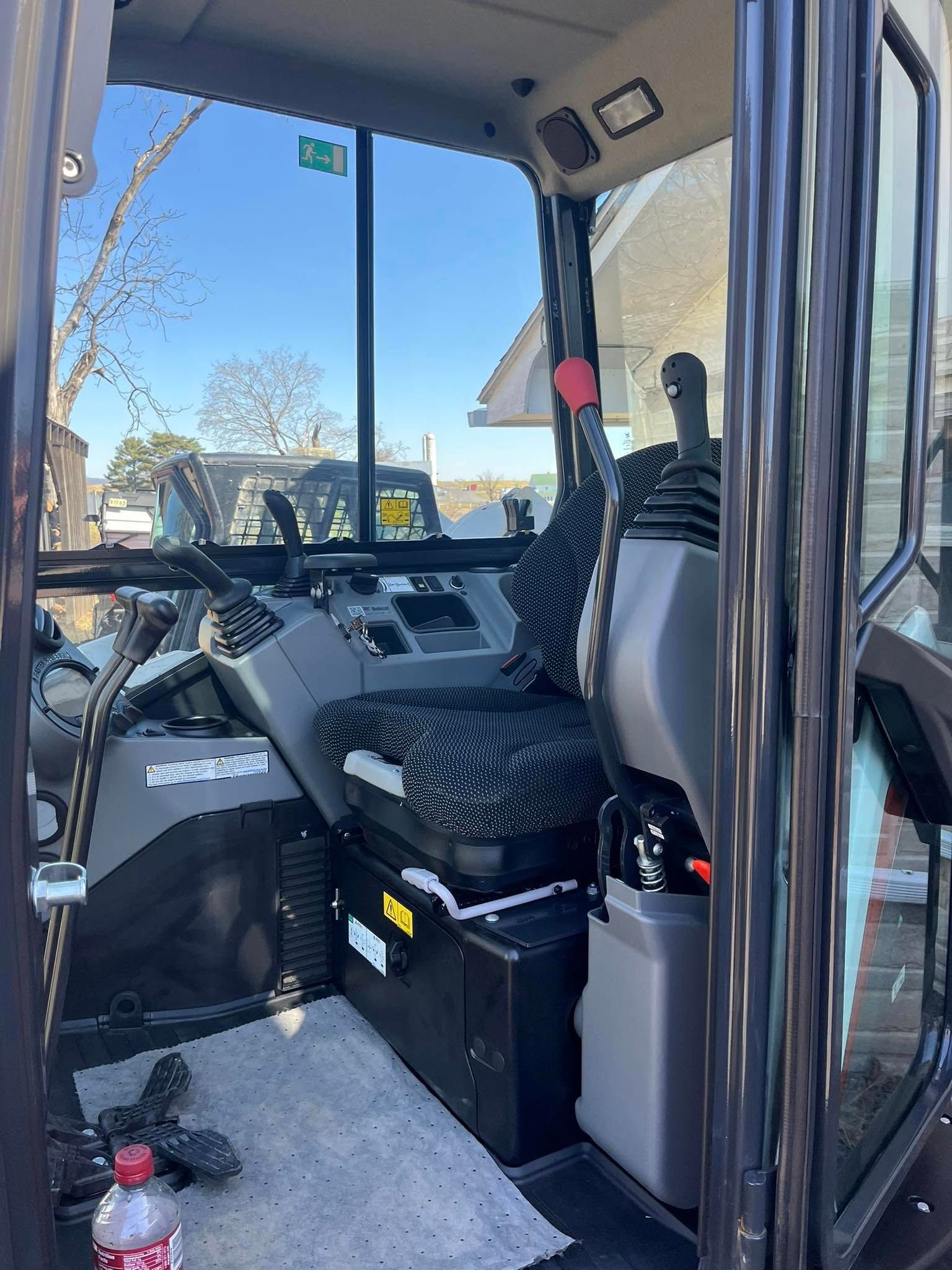 Interior of an excavator cab with seat, controls, and glass windows.