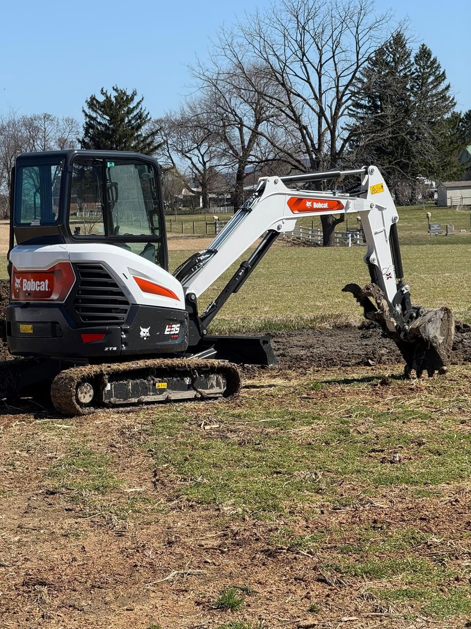 Bobcat mini excavator digging in a grassy field on a sunny day.