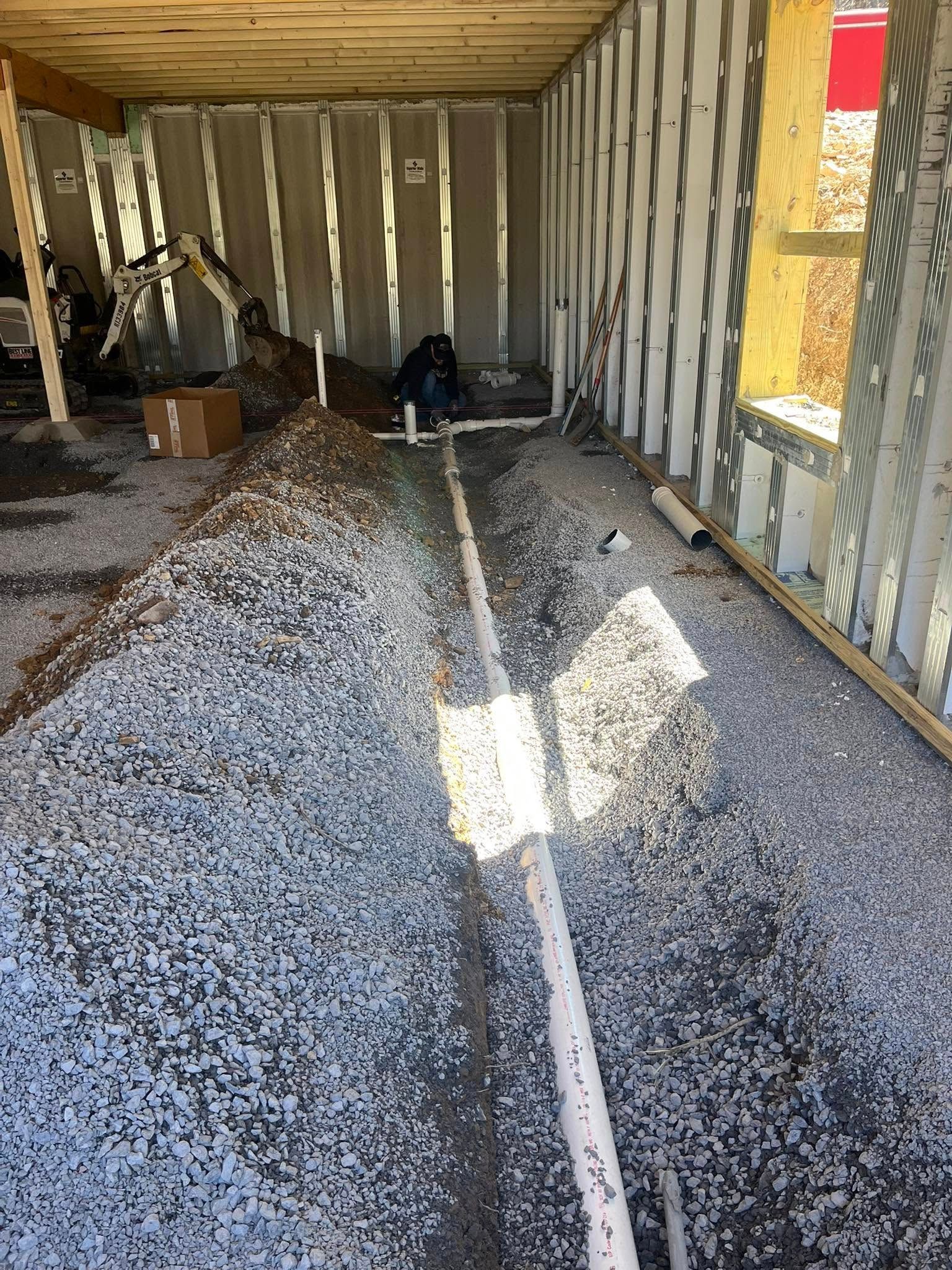 Interior view of a construction site showing gravel, plumbing pipes, and framing.