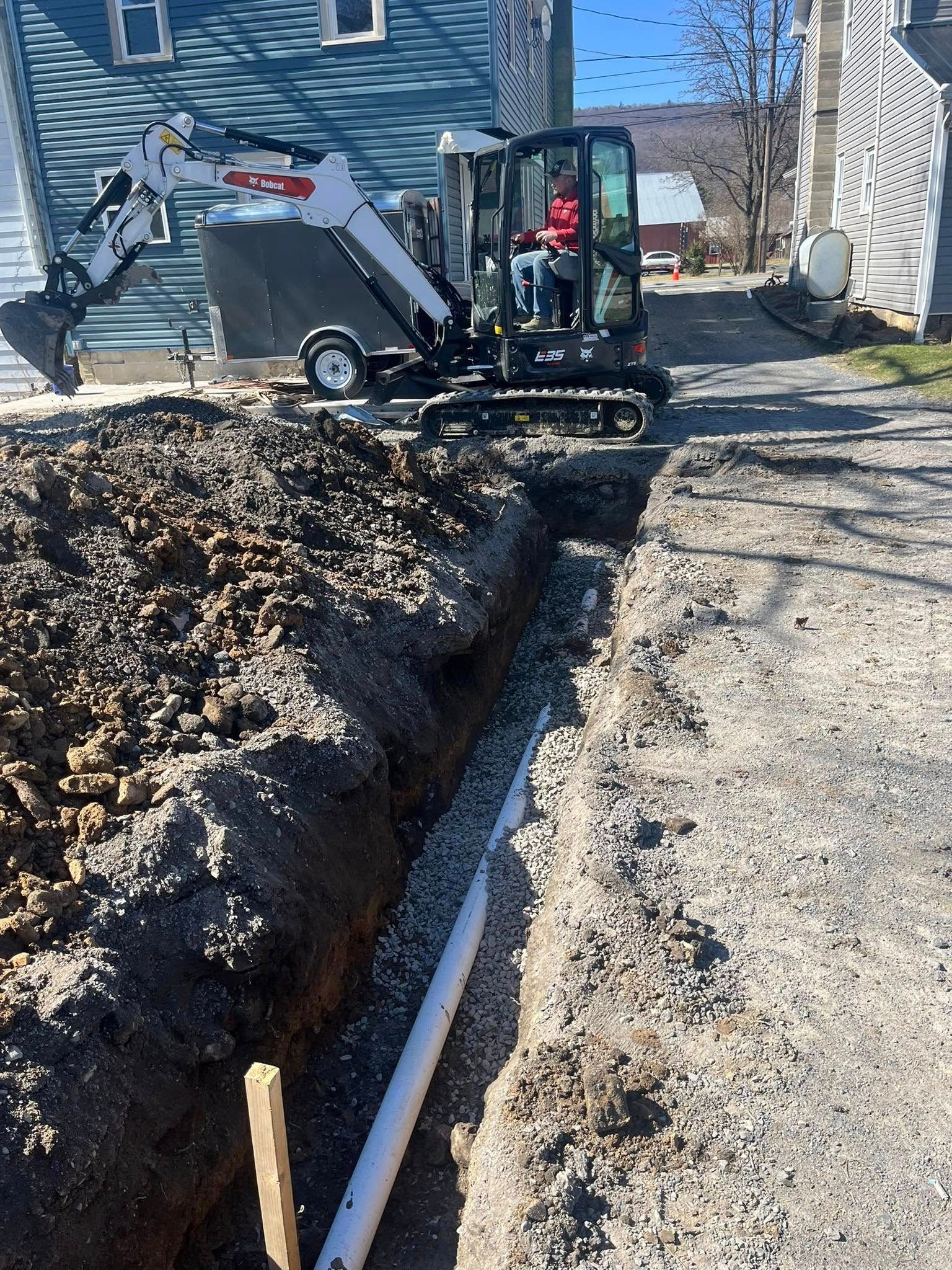 A small excavator in a trench on a sunny day. A person is inside the excavator.