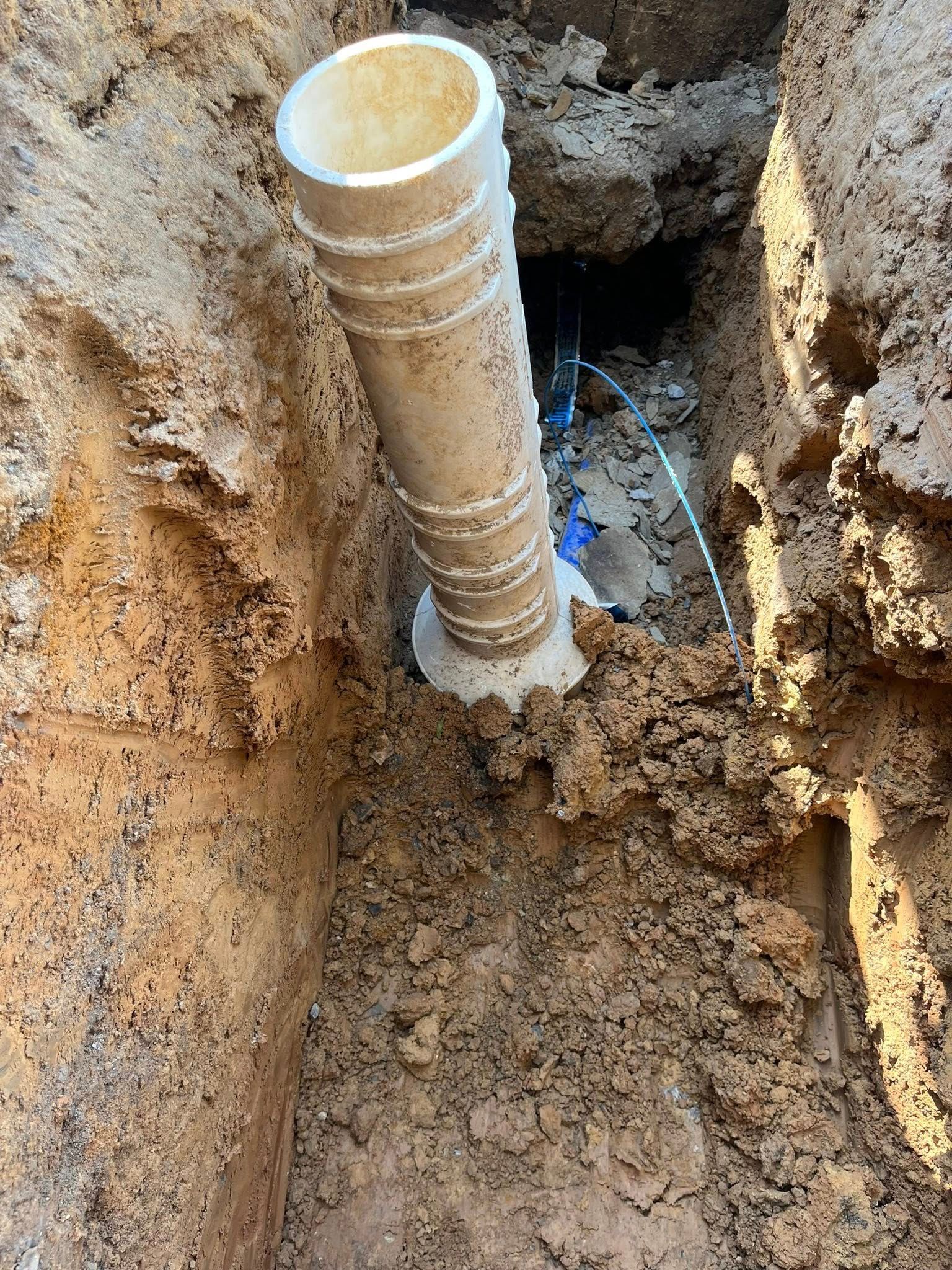 White PVC pipe in a brown soil trench. Construction or repair.