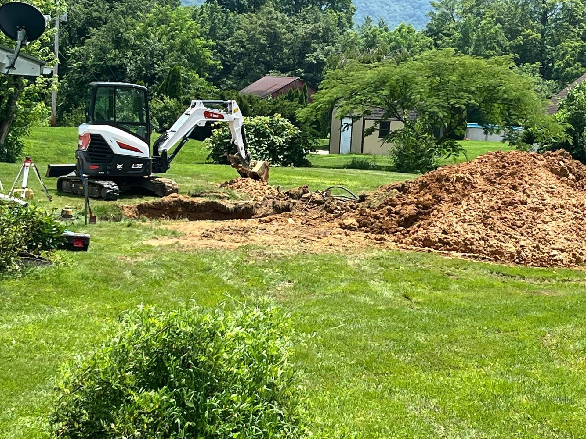 Bobcat excavator digging in a grassy yard, creating a pile of dirt.