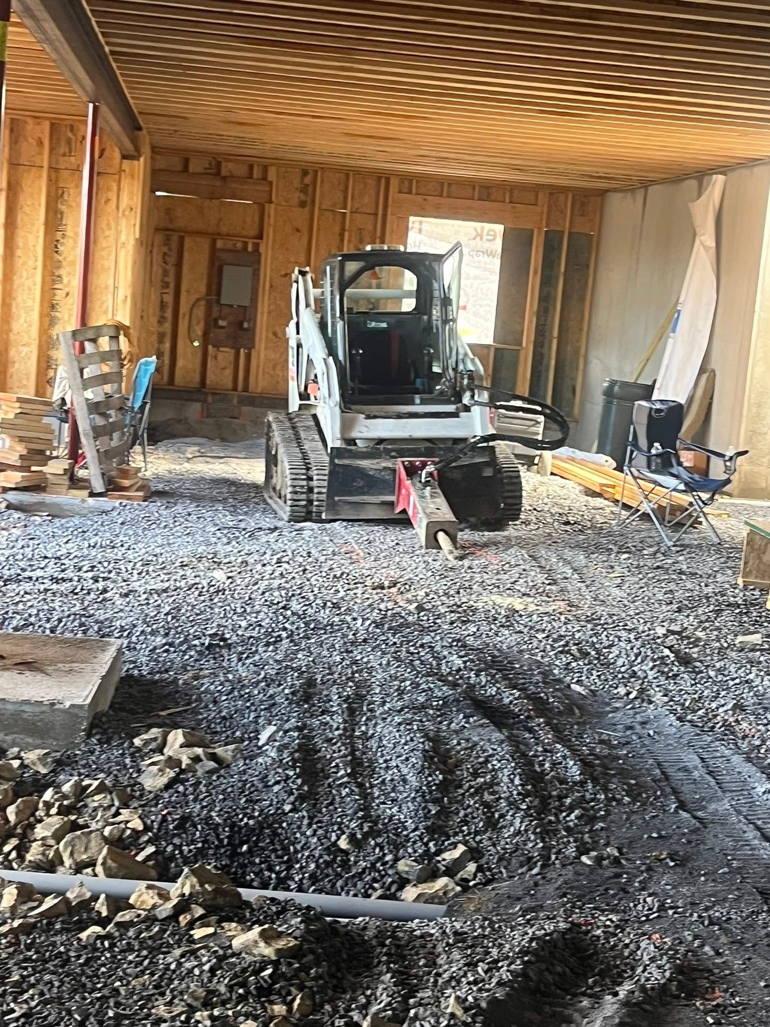 Bobcat on gravel in construction site, framed walls visible.