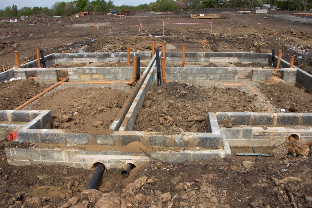Foundation of a building under construction, with concrete block walls and plumbing pipes.