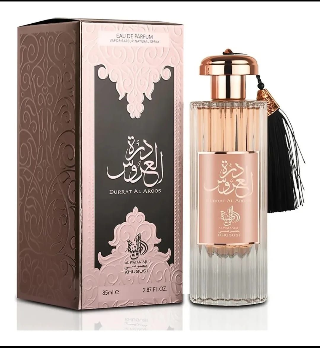 Frasco de perfume y caja. El frasco es de color oro rosa y transparente. La caja es marrón y rosa con texto en árabe.