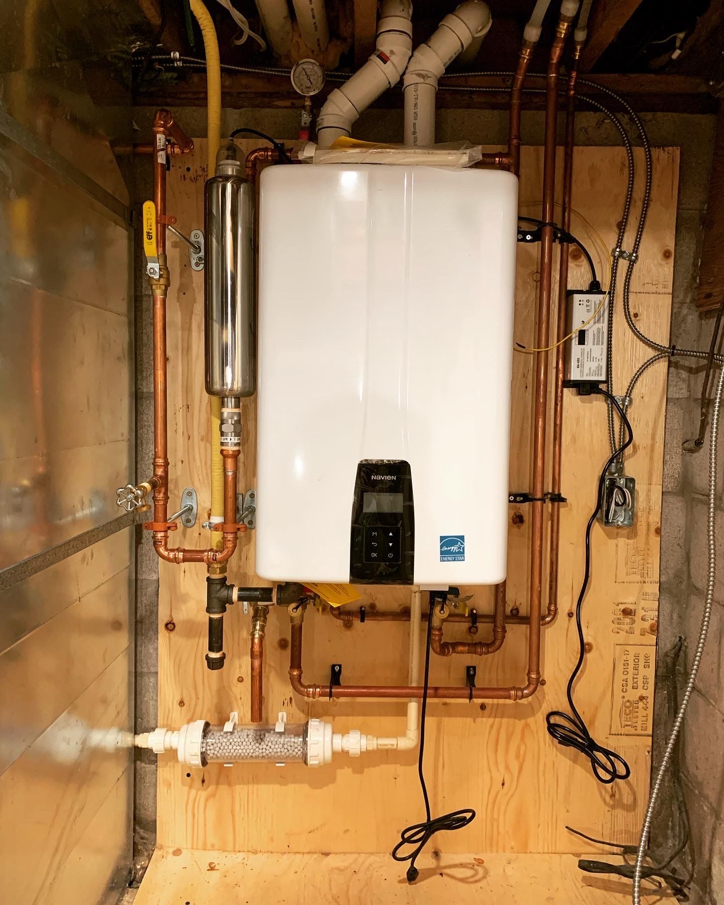 A white water heater is mounted to a wall with copper pipes.