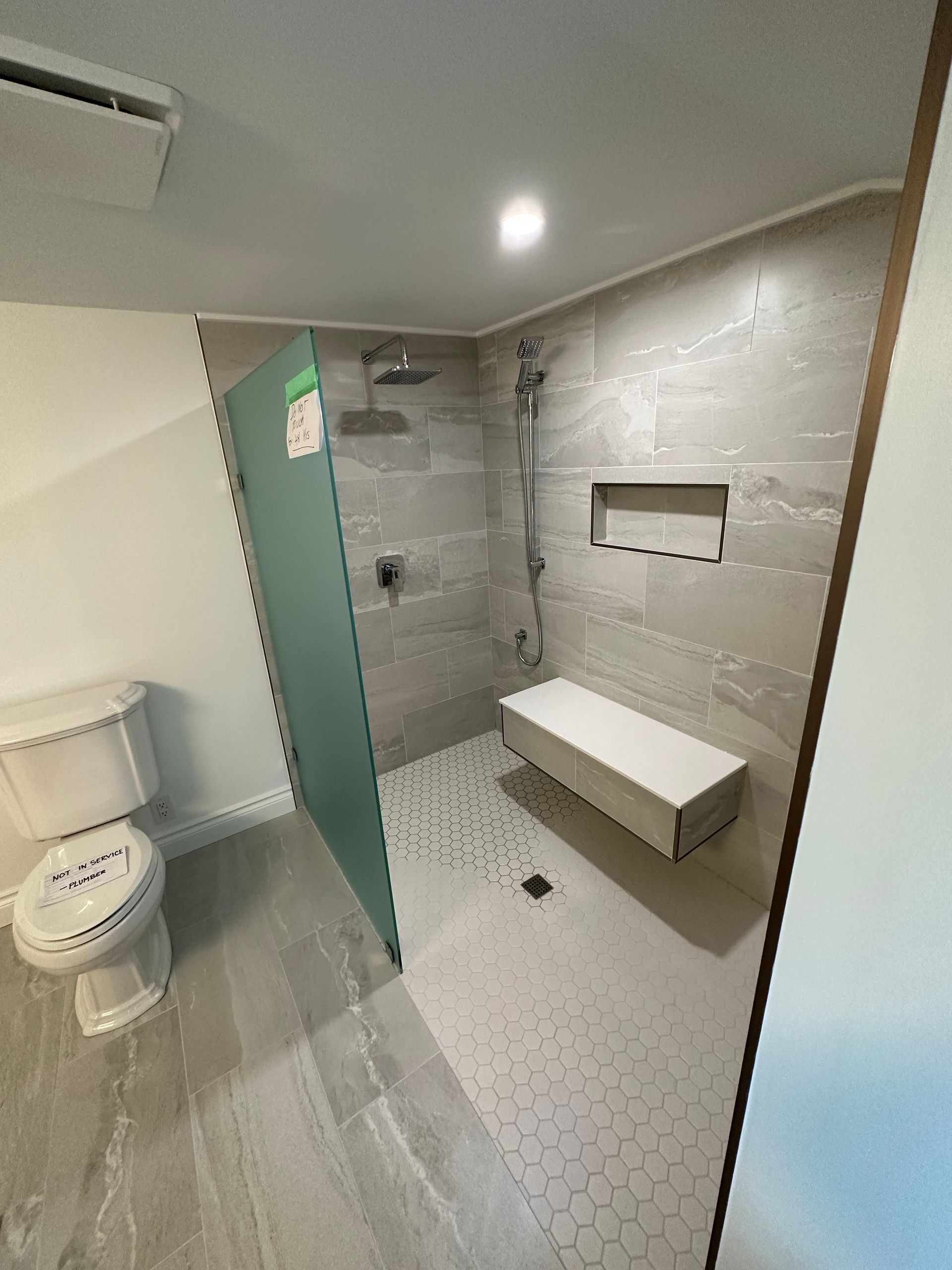 A bathroom with a toilet , shower and bench.