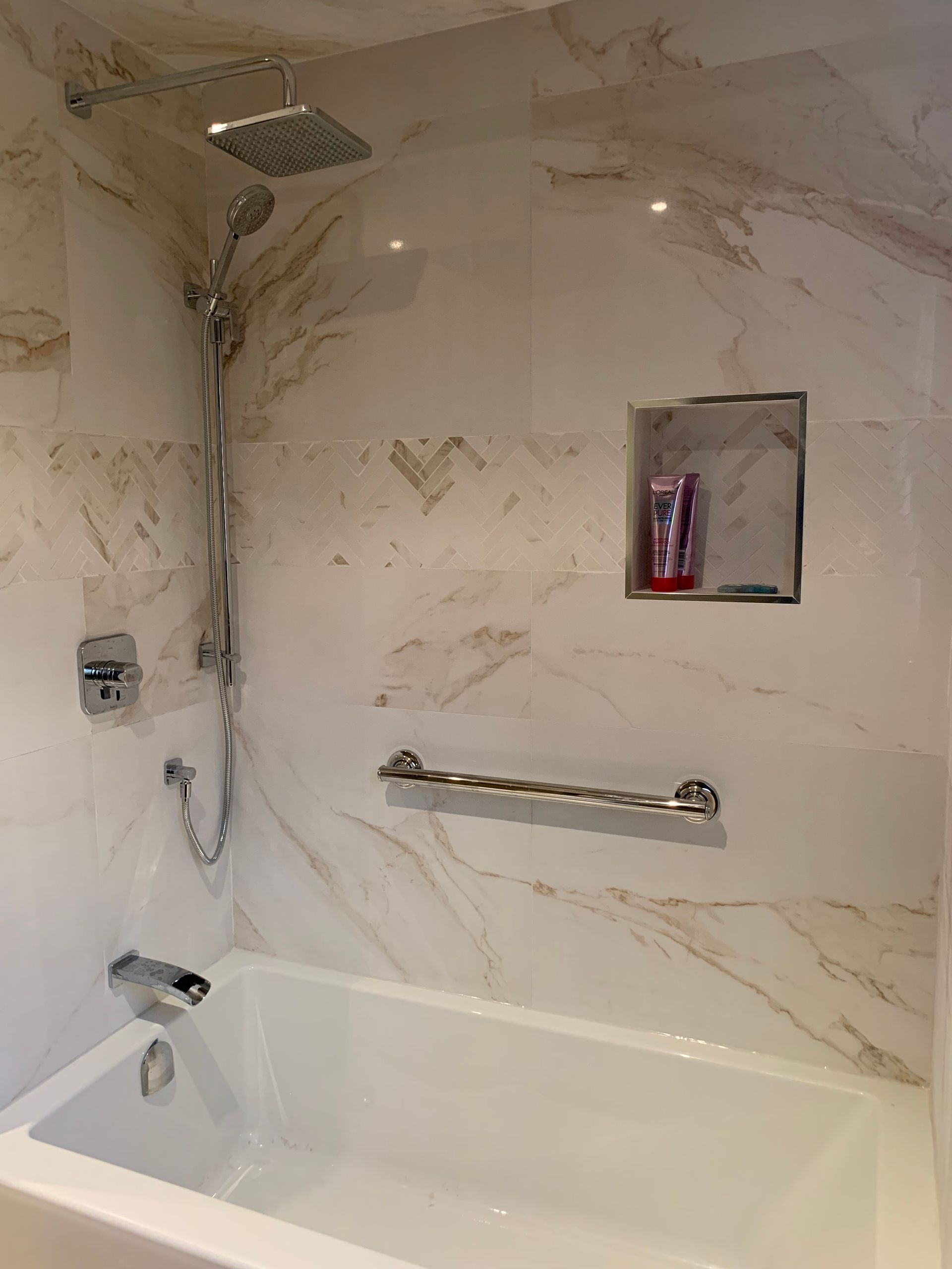 A bathroom with a bathtub , shower , and shelf.