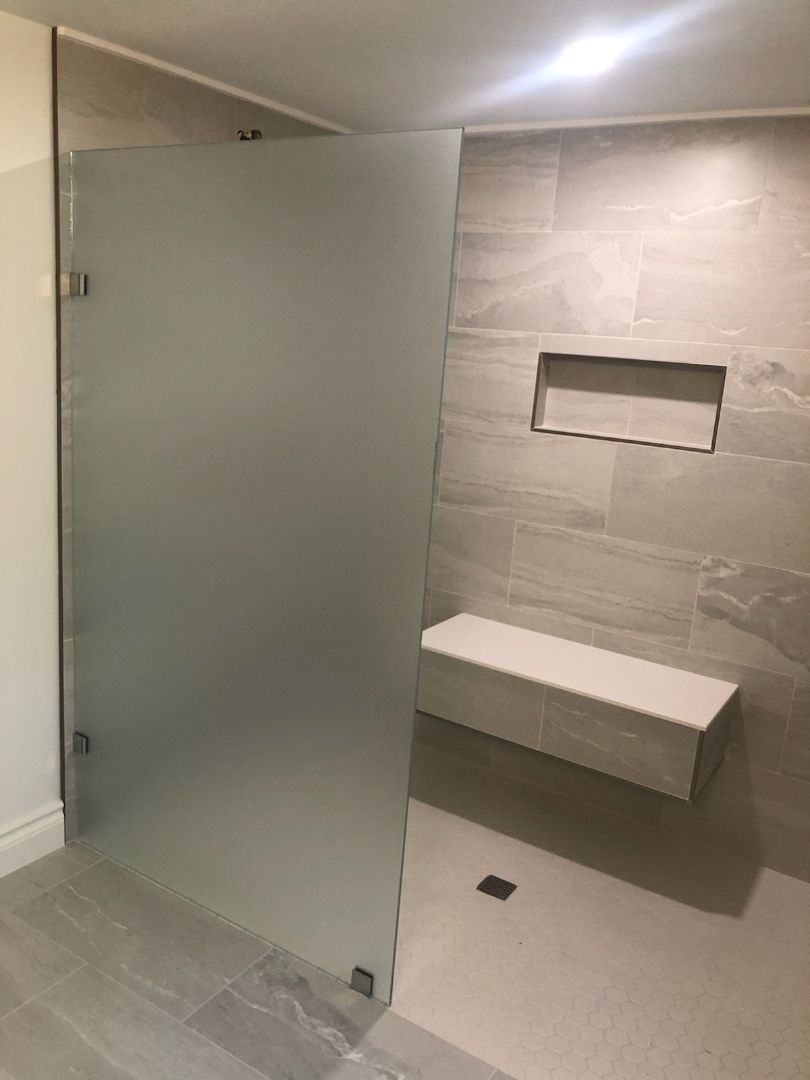 A bathroom with a glass shower door and a bench.