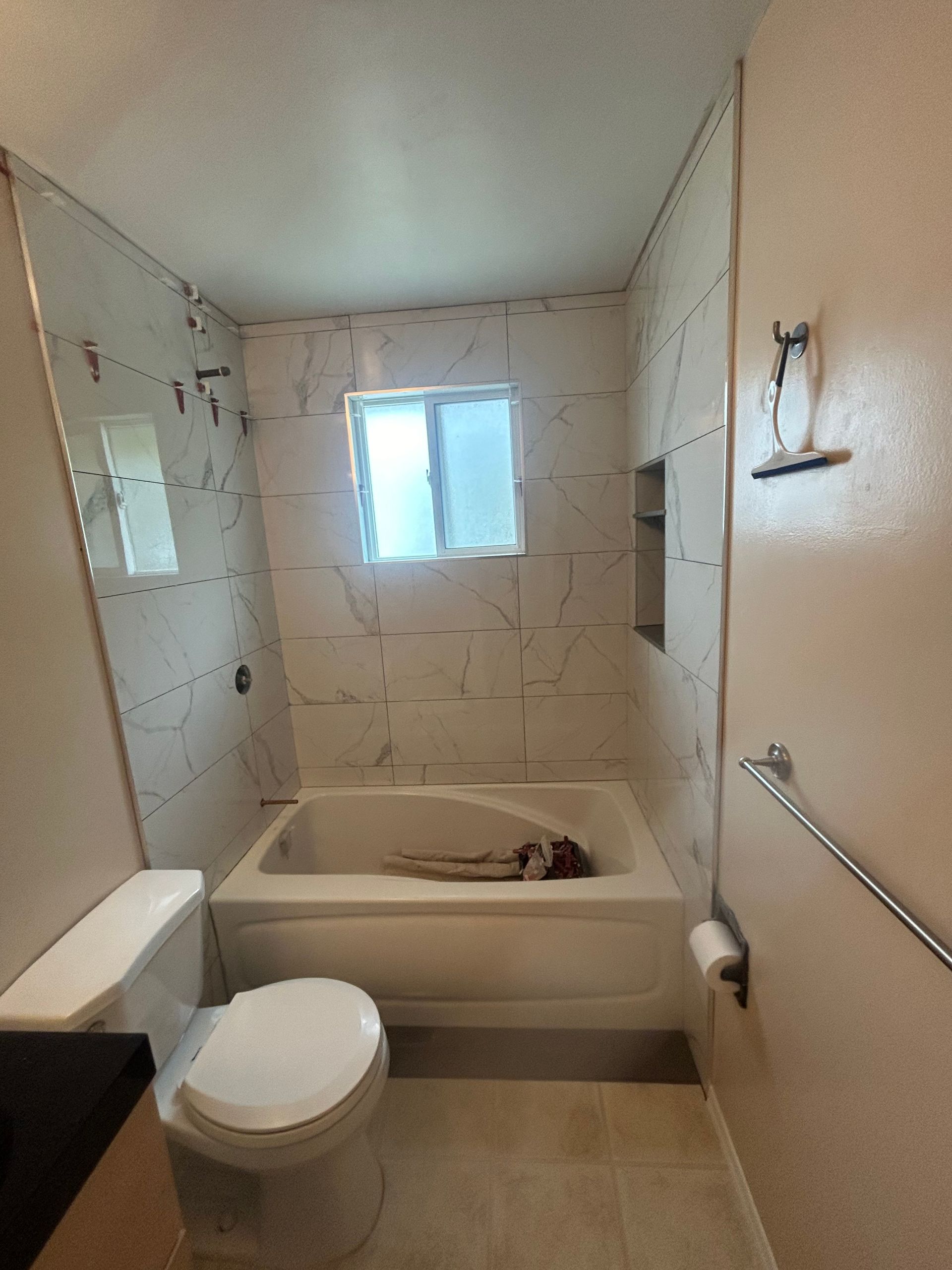 A bathroom with a toilet , tub , shower and window.