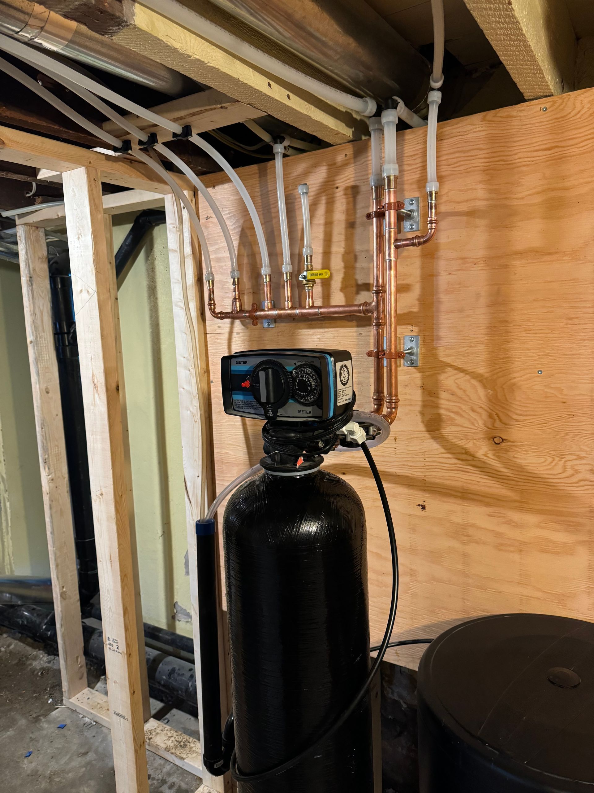 A water filter is sitting in a basement next to a copper pipe.