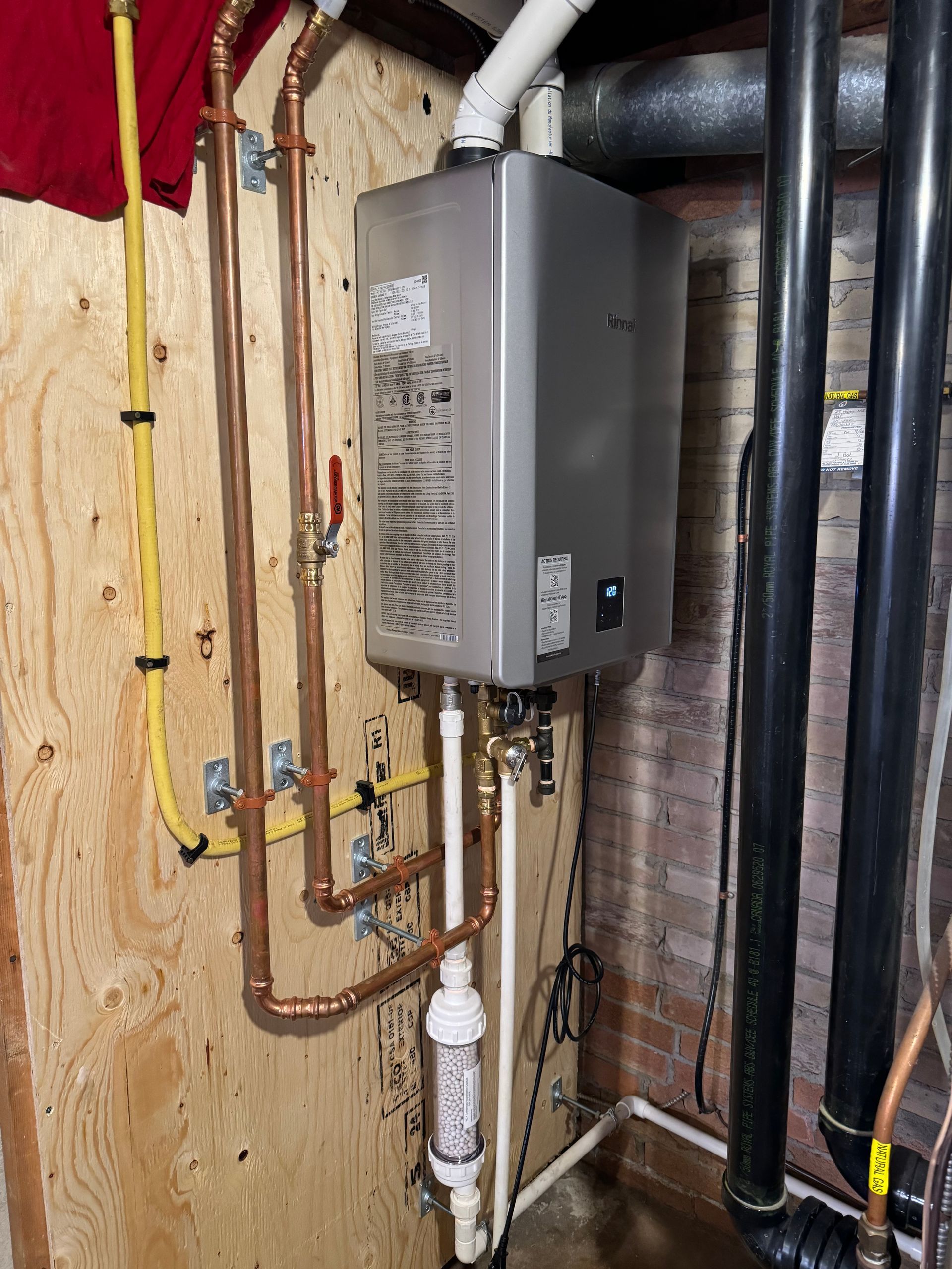 A water heater is installed in a basement next to copper pipes.