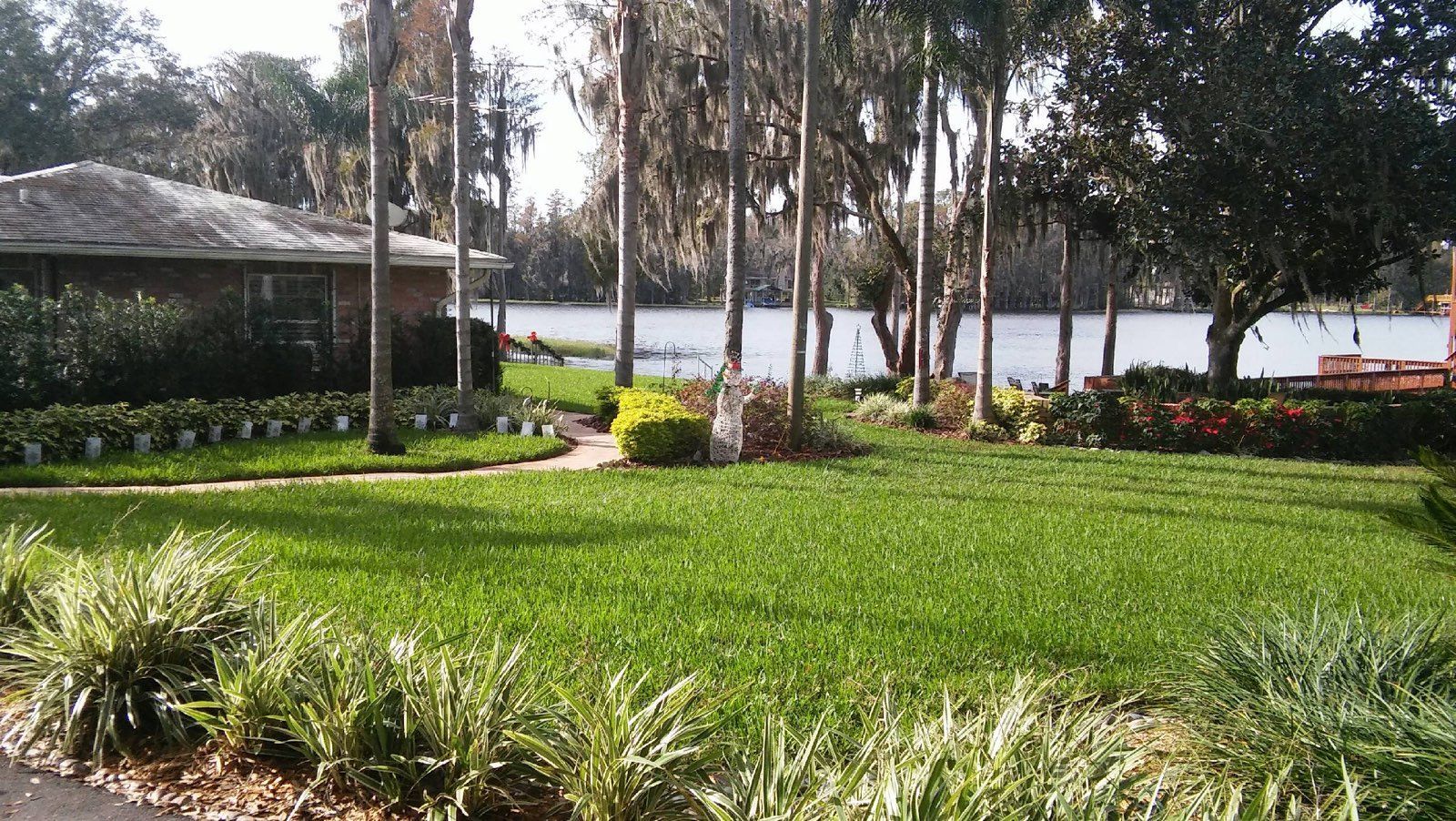 Lush green lawn leads to a lake with a house and trees in the background.