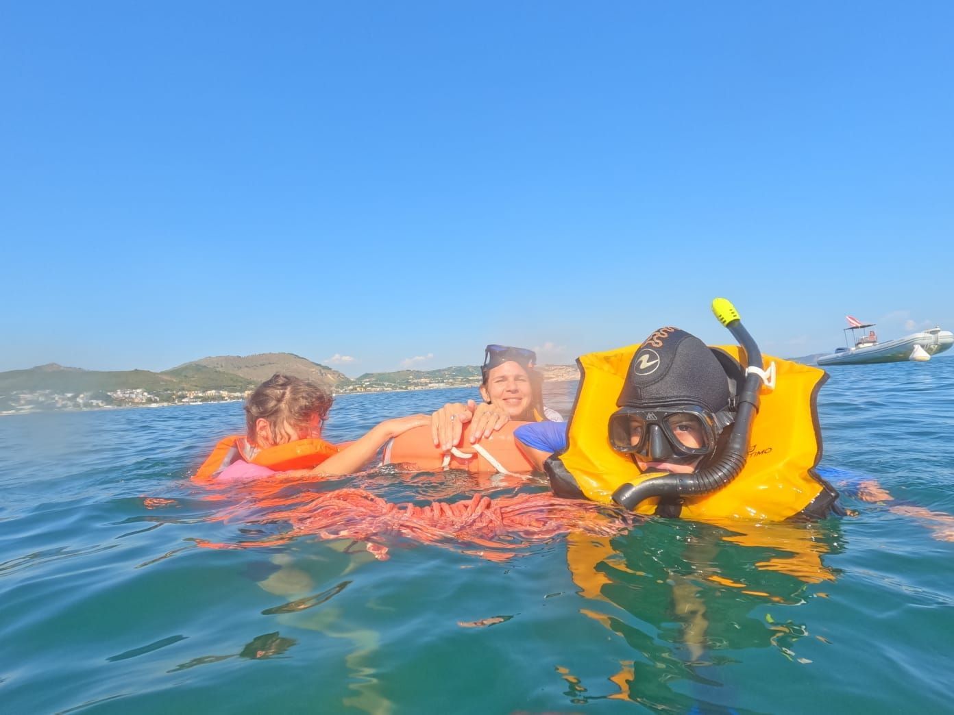 People snorkeling in clear water with a bright blue sky, wearing life vests and masks, near a coast.
