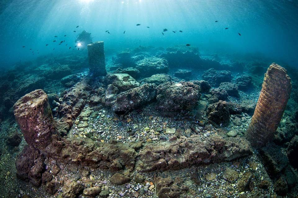 Underwater view of ancient ruins with a scuba diver exploring.