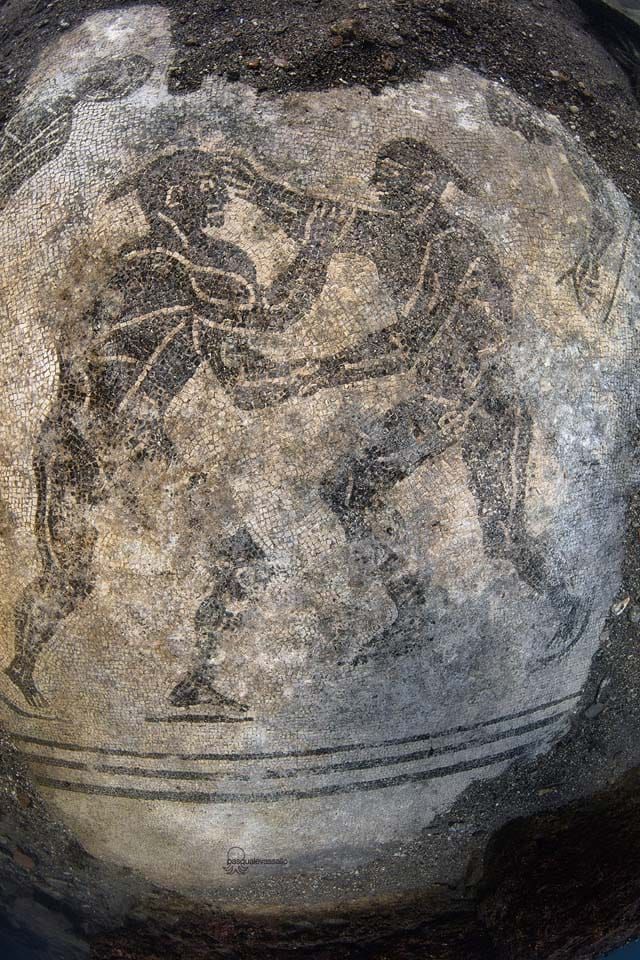 Ancient fresco of two men boxing in a circular arena, black outline on a gray background.