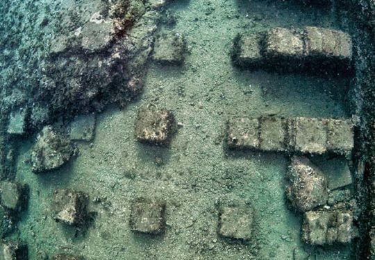 Underwater view of submerged stone blocks and columns, possibly ruins.