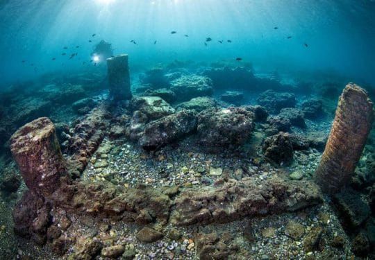 Underwater view of ancient ruins with columns and a diver.