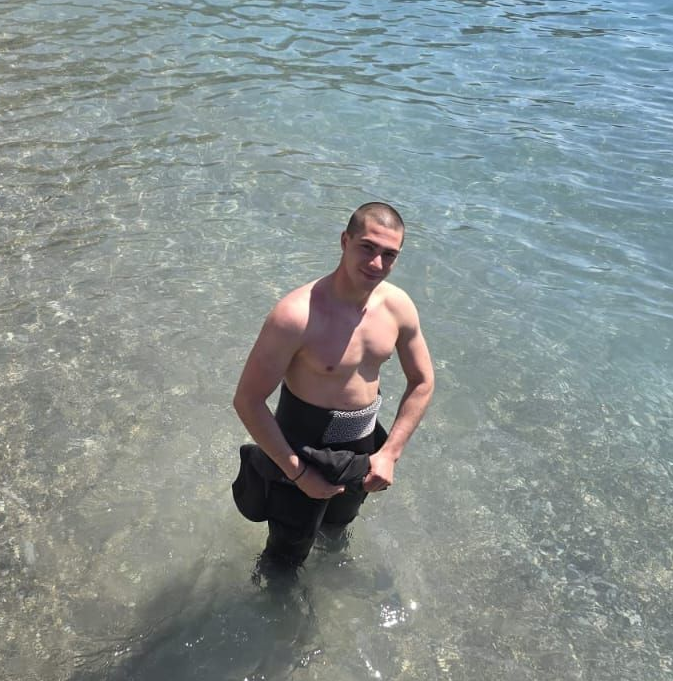 Man in wetsuit standing in clear water, smiling.