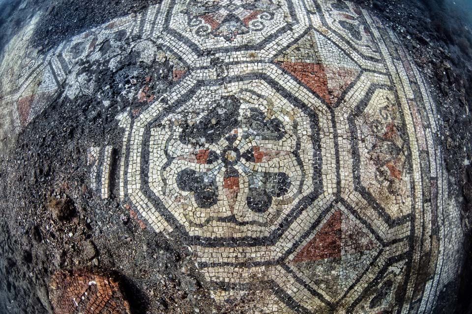 Underwater view of ancient mosaic tile floor with geometric patterns and floral center.