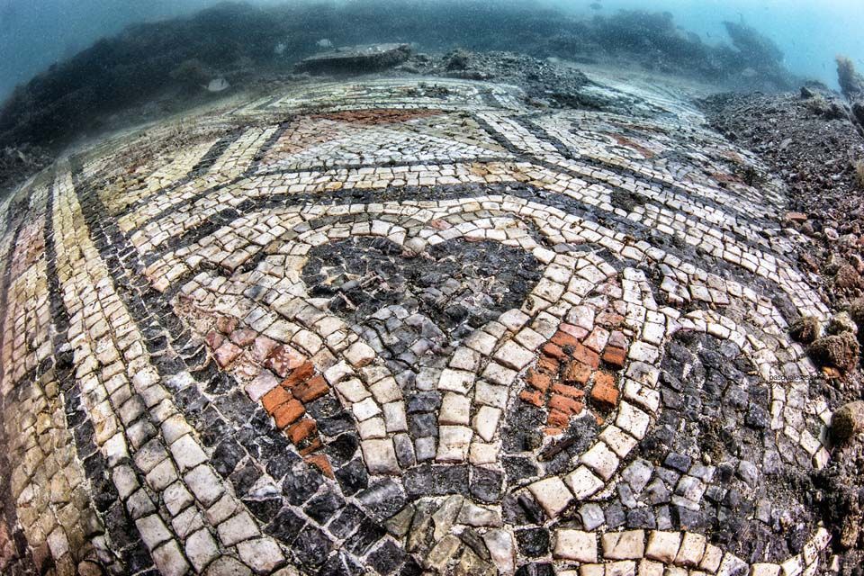 Underwater view of an ancient mosaic floor, featuring intricate geometric patterns with white, black, and red tiles.