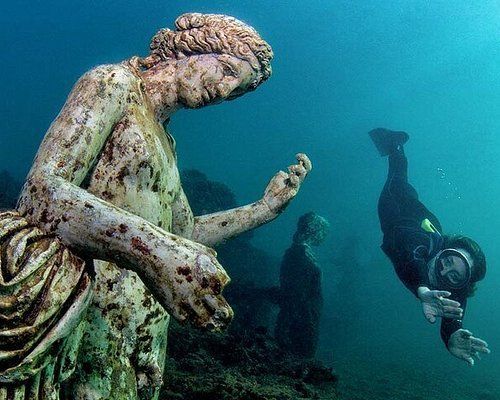 Underwater statues with diver; statues are weathered and greenish, diver swims.