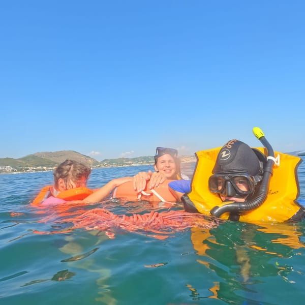 Three people snorkeling in ocean water, wearing life vests and masks, under a clear blue sky.