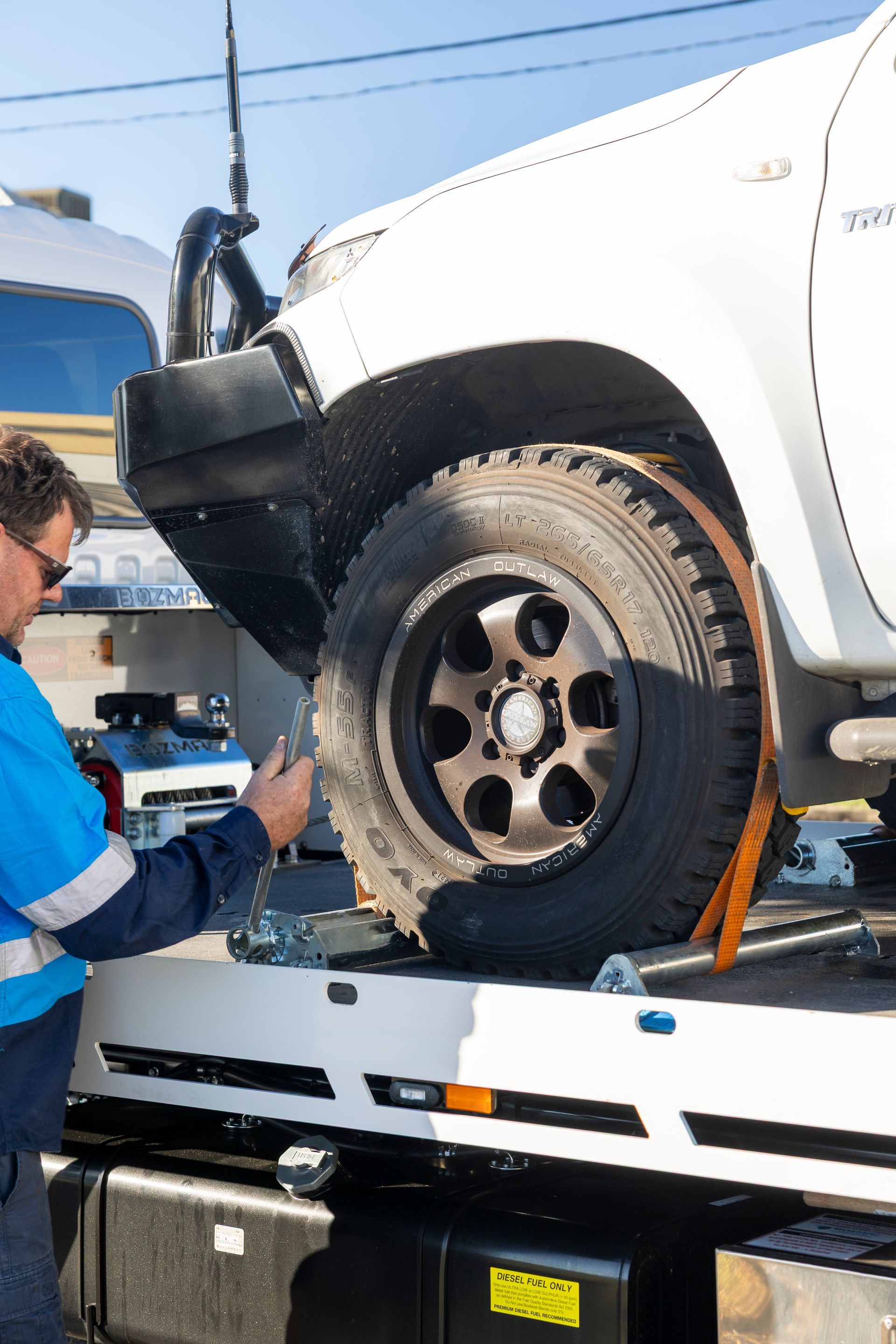 Tow truck operator securing a white truck with an orange strap. Sunny outdoor setting.— Perlyn Towing  in Emerald, QLD