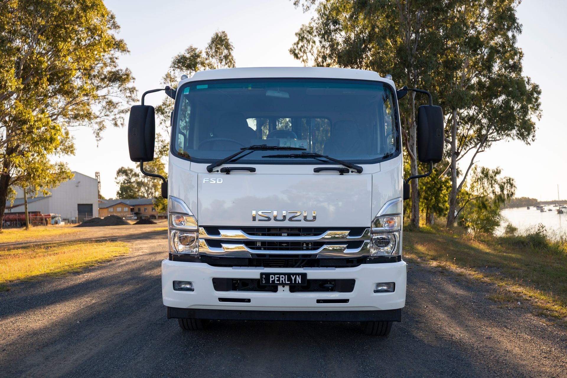 White Isuzu truck parked on a road, facing the camera, with trees and a body of water in the background.— Perlyn Towing  in Emerald, QLD