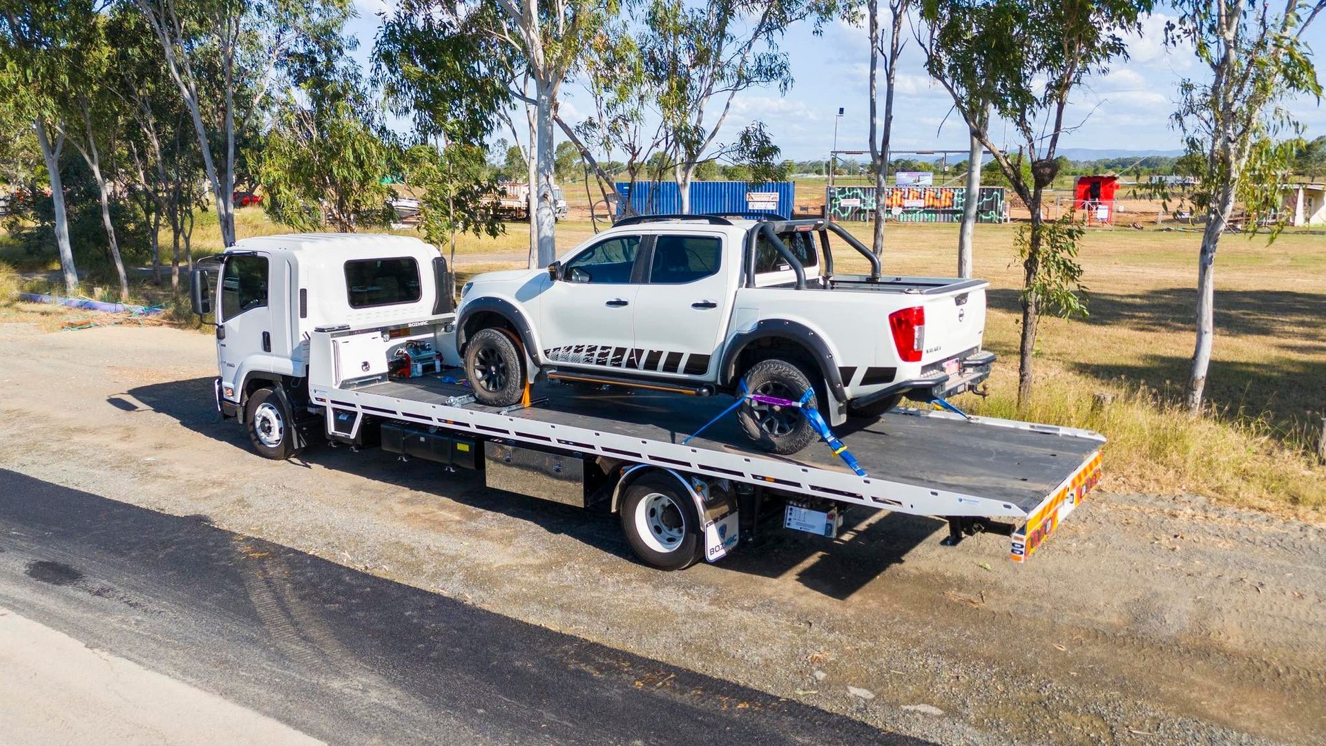 White pickup truck secured on the flatbed of a tow truck, outdoors.