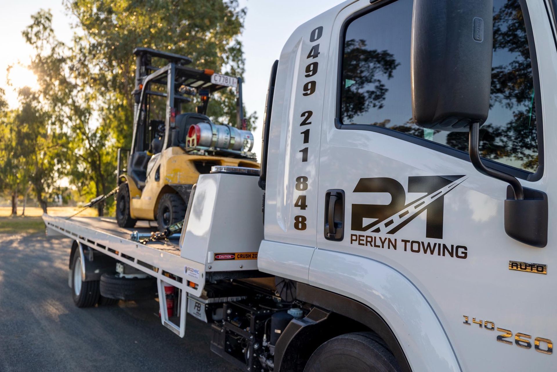 A flatbed tow truck carrying a yellow forklift. Ferlyn Towing logo is visible.— Perlyn Towing  in Emerald, QLD
