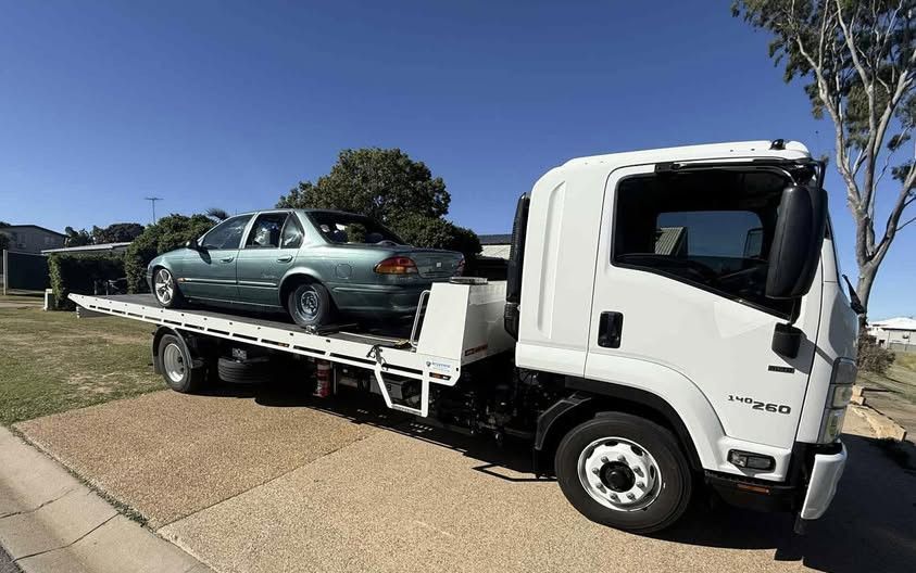 A light green sedan on a white flatbed tow truck, parked on a brick driveway under a blue sky.— Perlyn Towing in Rockhampton City, QLD