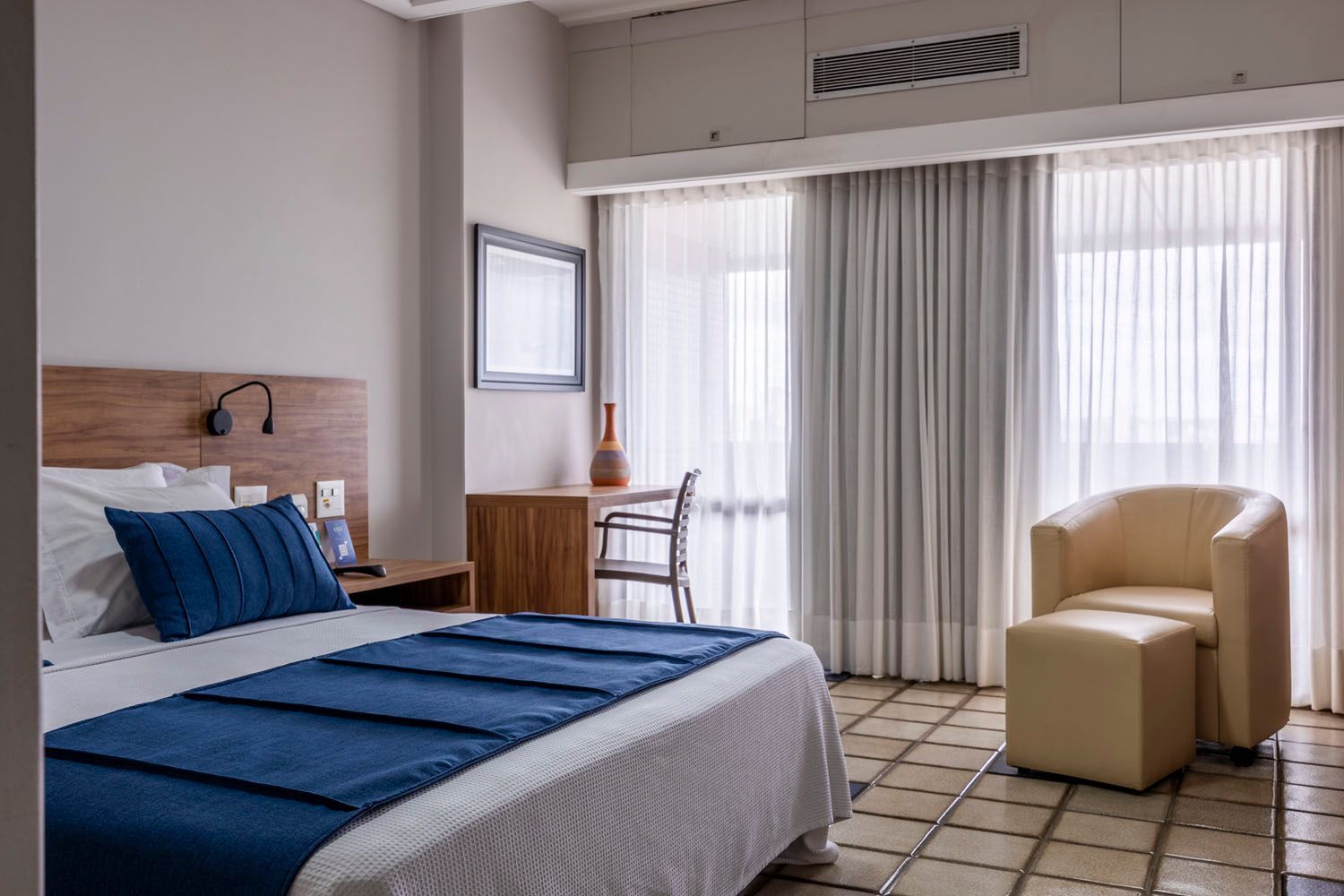 Um quarto de hotel com uma cama, cadeira, escrivaninha e janela.