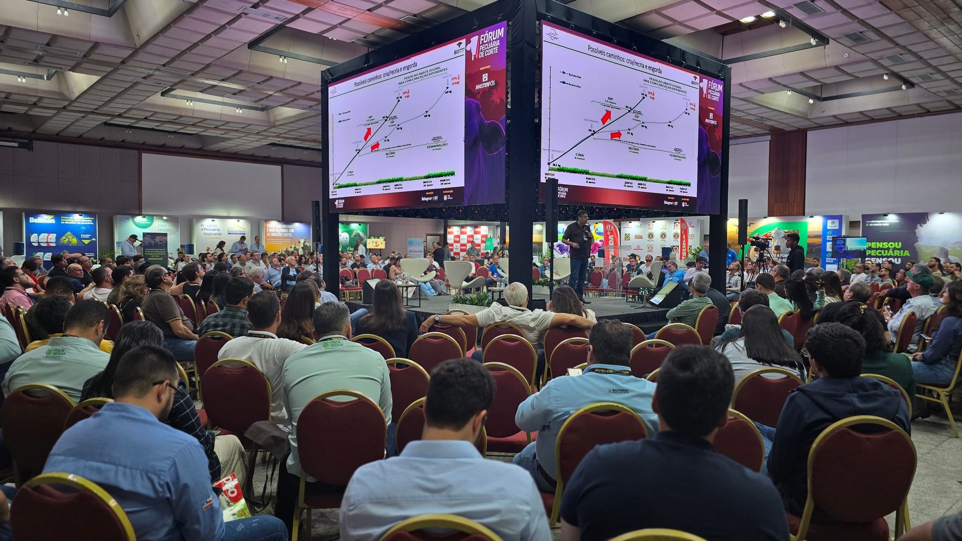 Um grande grupo de pessoas está sentado em uma sala de conferências assistindo a uma apresentação.