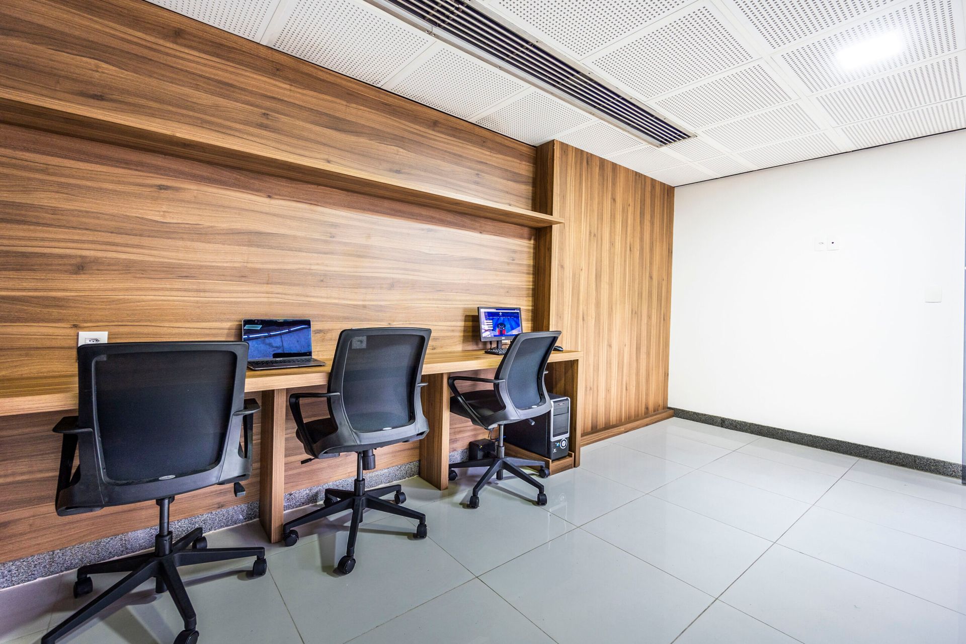 Uma sala com três mesas e cadeiras com computadores sobre elas.