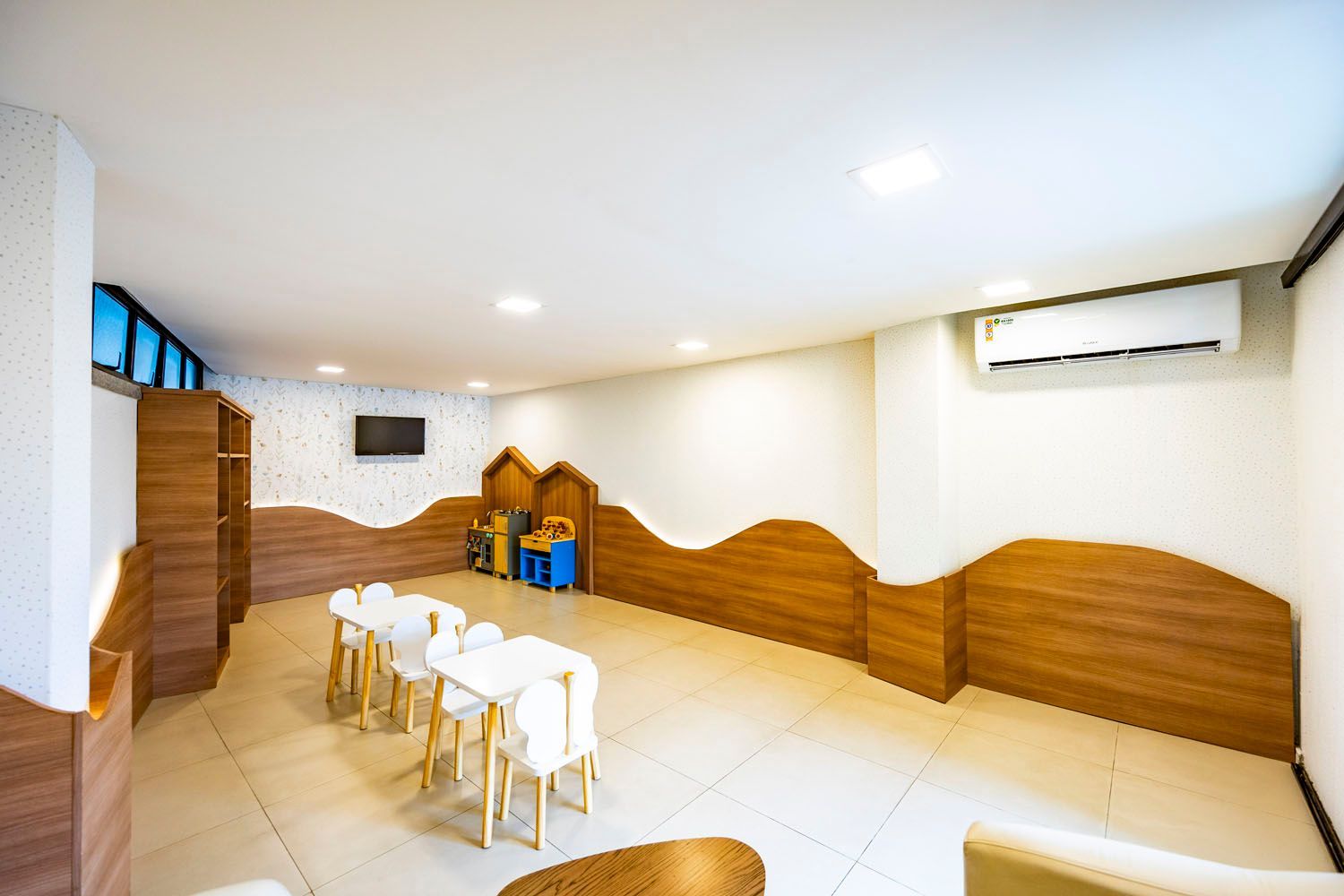 Uma sala com mesas e cadeiras e uma televisão na parede.