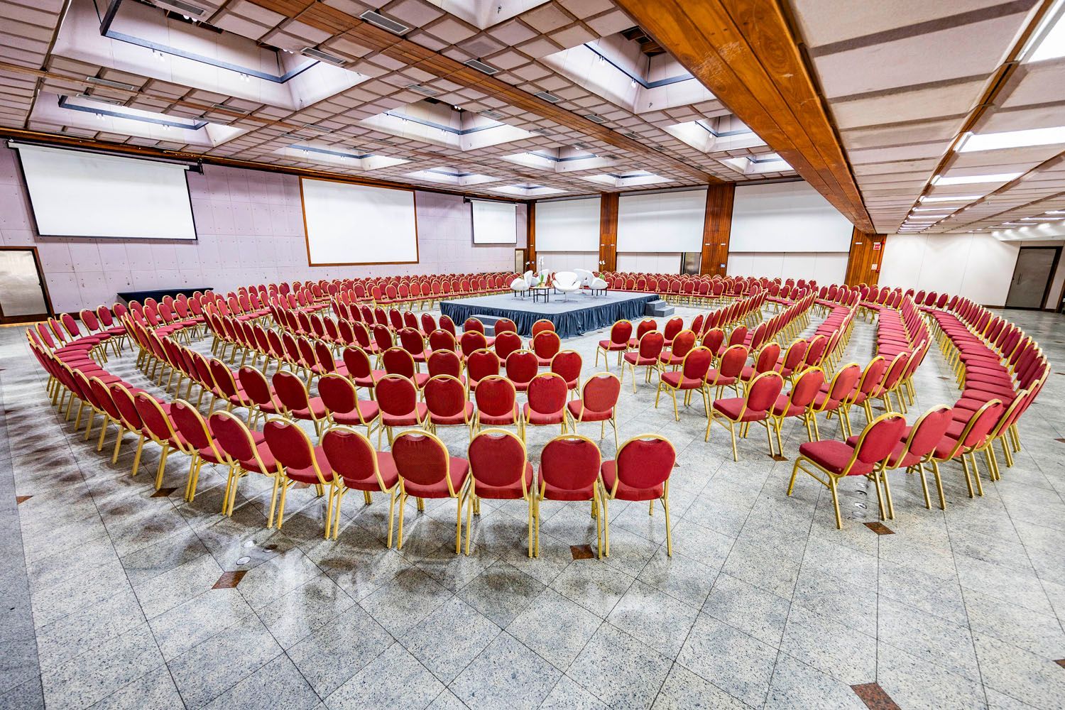 Fileiras de cadeiras vermelhas estão dispostas em círculo em uma sala grande.