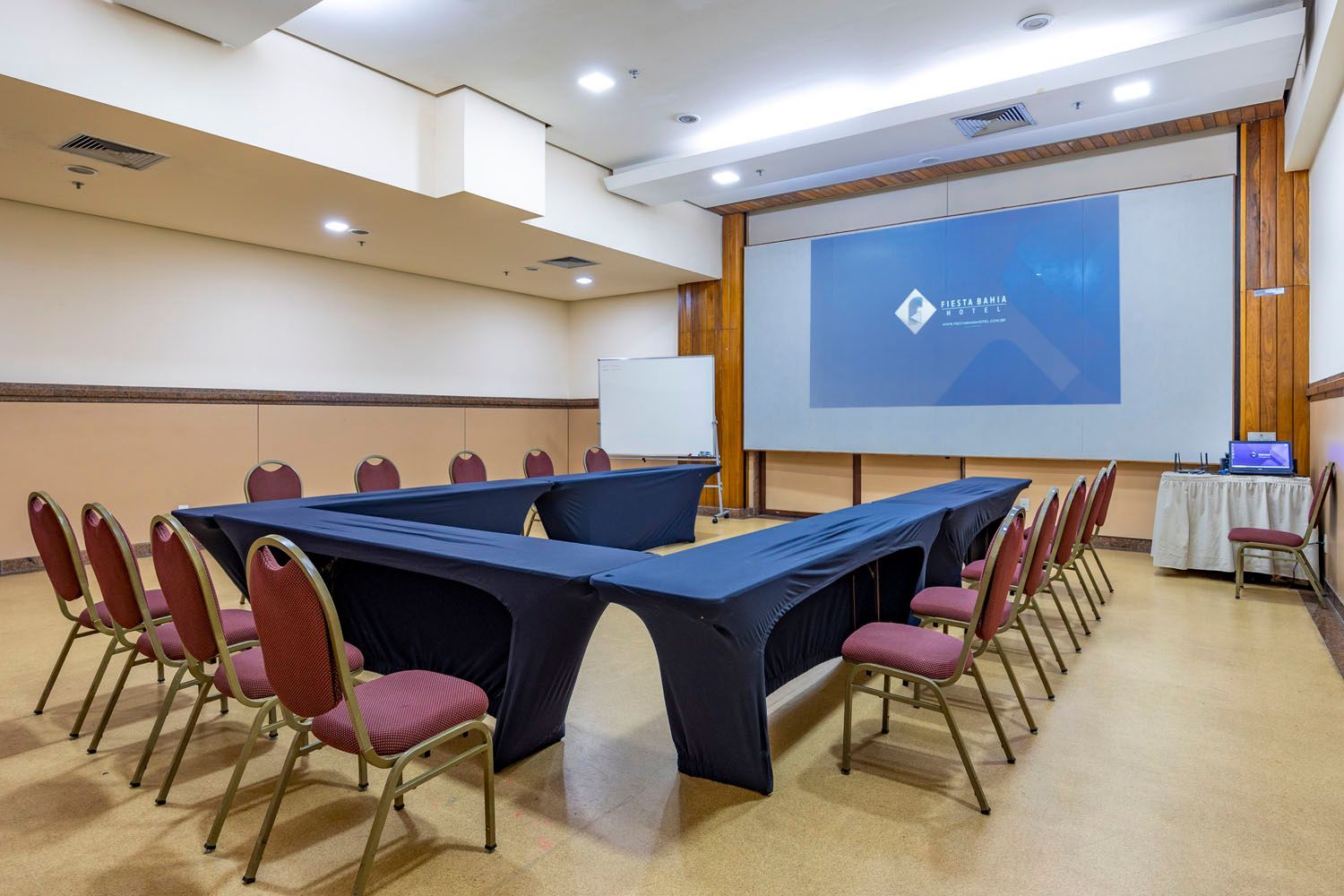Uma sala de conferências com mesas e cadeiras e uma tela grande.
