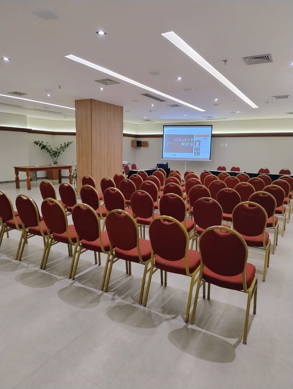 Uma sala grande com fileiras de cadeiras vermelhas e uma tela de projetor