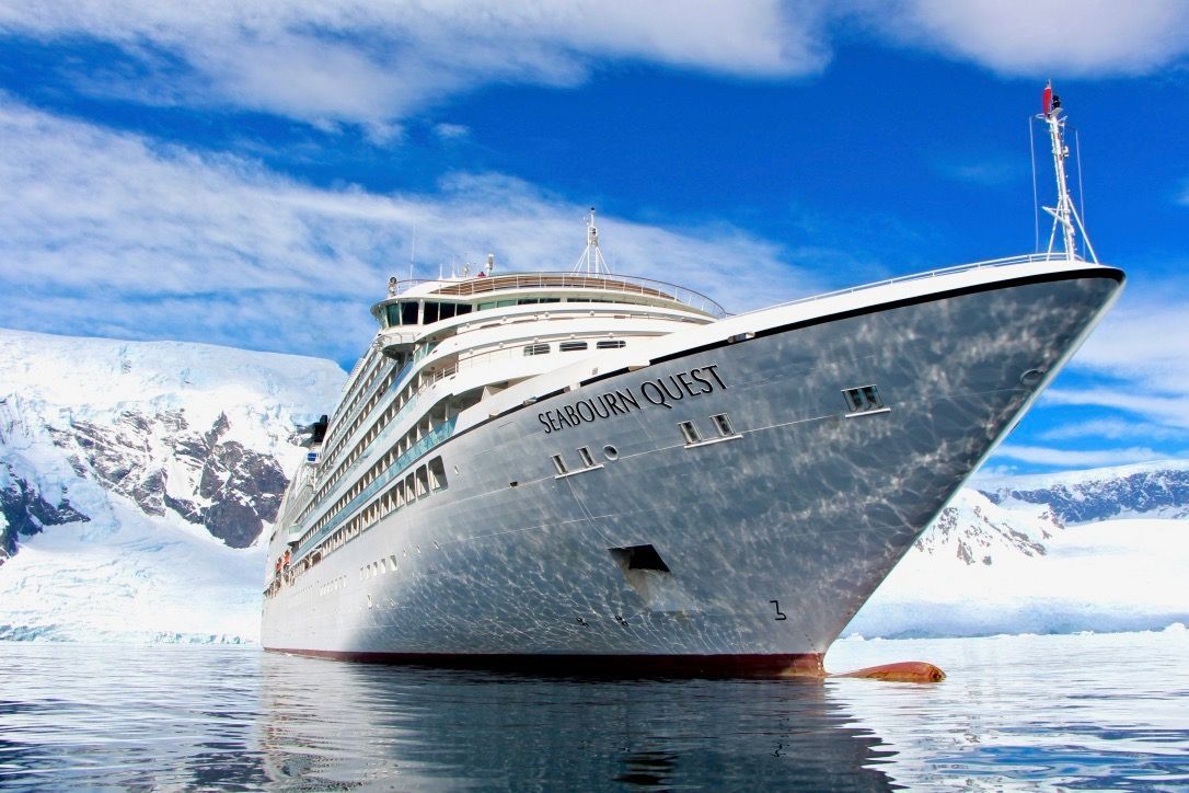 A large cruise ship is in the water near a snowy mountain