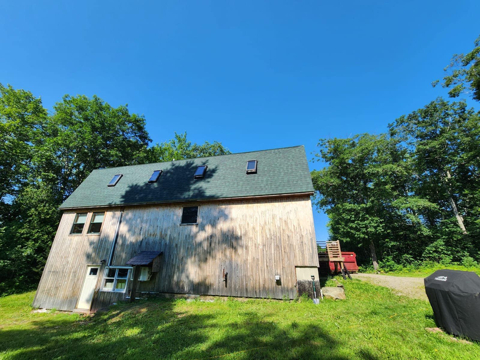A large wooden barn with a green roof is sitting in the middle of a grassy field.