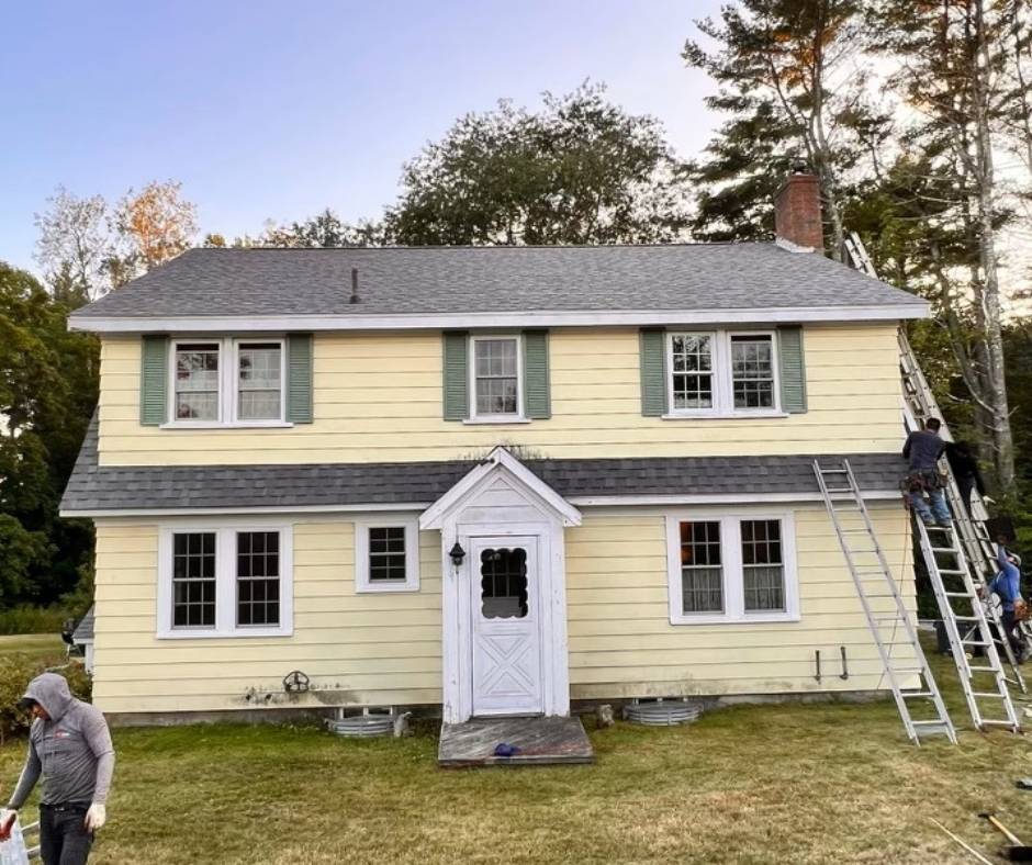A yellow house with a black roof and green shutters