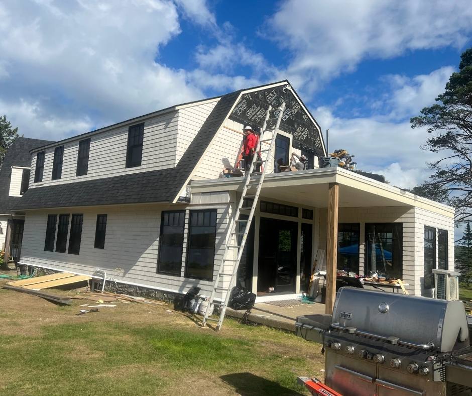 A man on a ladder is working on the roof of a house.